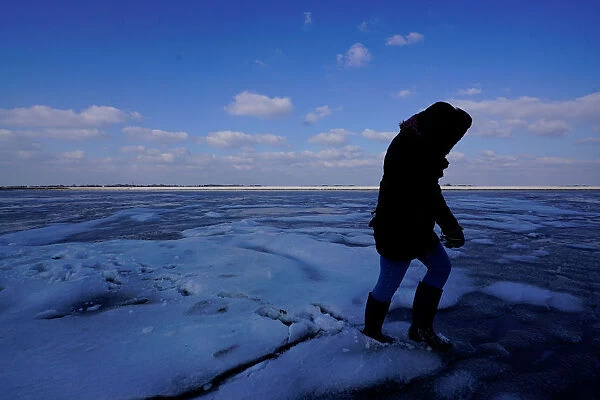 A person walks on fractured ice on the Wadden Sea during the low tide near the island of