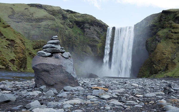 A pile of rocks stand in front of a waterfall in Skogarfoss, Iceland