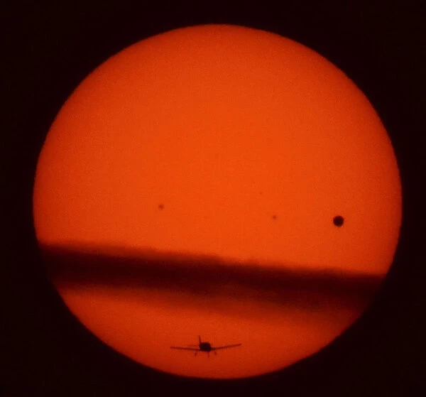 A plane flies under a thin layer cloud crossing the sun as Venus (R