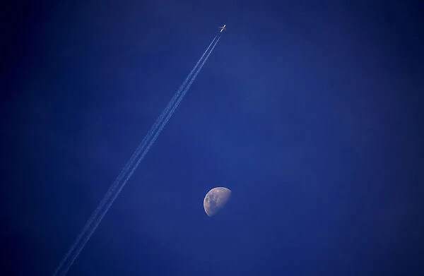 A plane leaves a vapor trail as it flies past the moon above the town of Gunnedah