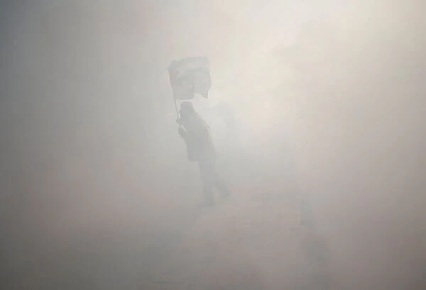 Protester holds a Palestinian flag as he stands amidst tear gas fired by Israeli troops