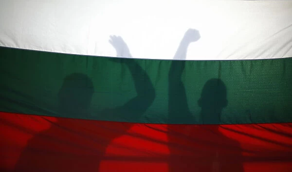 Protesters cast their shadows on a Bulgarian flag as they shout anti-government slogans