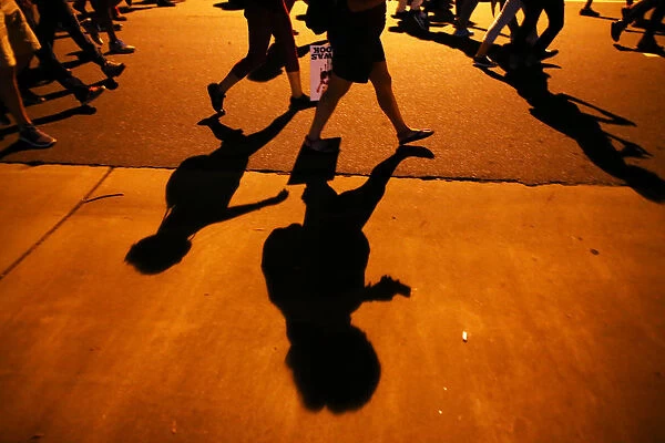 Protesters shadows mark the sidewalk as they march during another night of protests