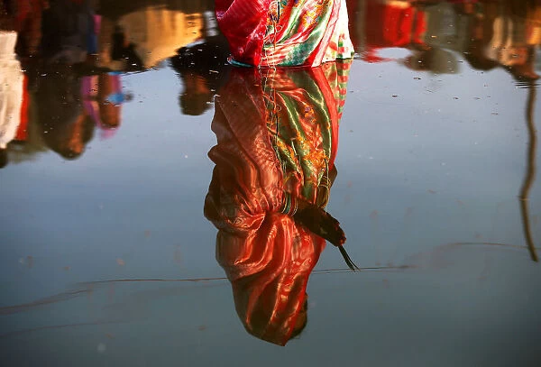 The reflection of a woman is seen in the waters of the Sabarmati River as she worships