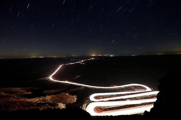 The road is illuminated by the headlights of cars being driven through Ramon Crater near