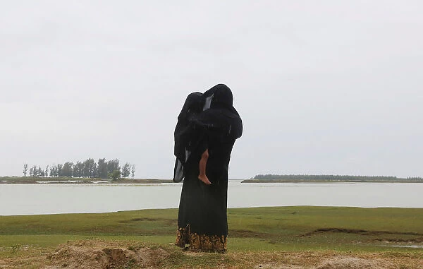 A Rohingya refugee woman protects her son from rain as she looks towards the beach after