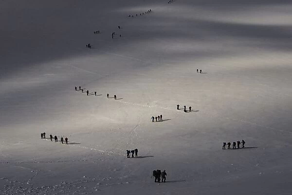Roped parties of climbers walk on a glacier marking the border between Switzerland