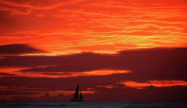 A sailboat passes in front of clouds lit up by the sunset sky off Waikiki in Hawaii, U. S