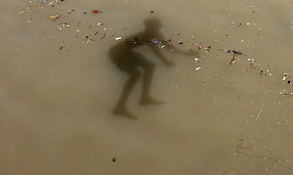 The shadow of a boy is seen as he jumps into the Ganges river to cool off on a hot summer