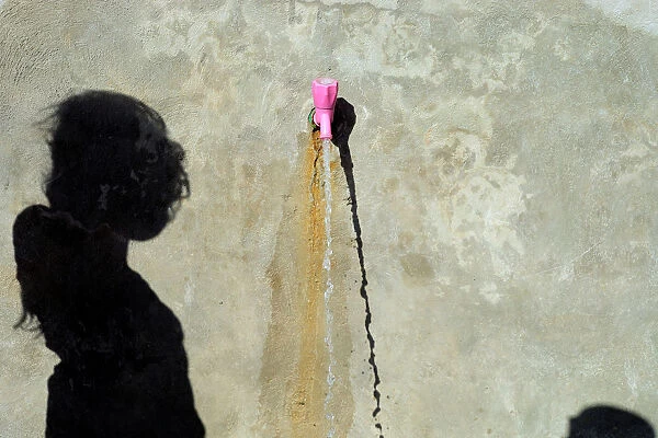The shadow of an internally displaced girl who fled Raqqa is cast at the water point