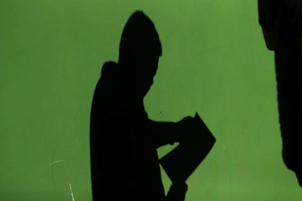 The shadow of a man is cast on a wall as he checks his documents after leaving a