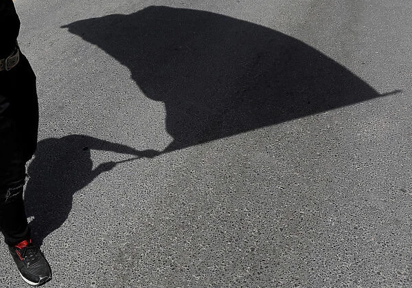 The shadow of a protester holding a flag is seen on the road during a May Day rally