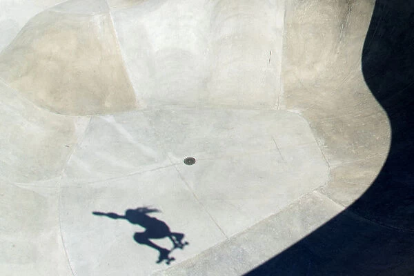 The shadow of a skateboarder is cast at the bottom of a cement bowl