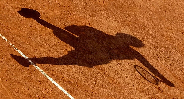 THE SHADOW OF A TENNIS PLAYER AS HE SERVES IS CAST ON THE CLAY