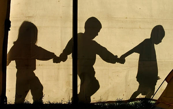 The shadows of children walking hand in hand are seen on a tent at a temporary refuge