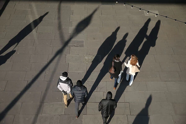 The shadows of pedestrians are cast on the pavement as they walk along the South Bank