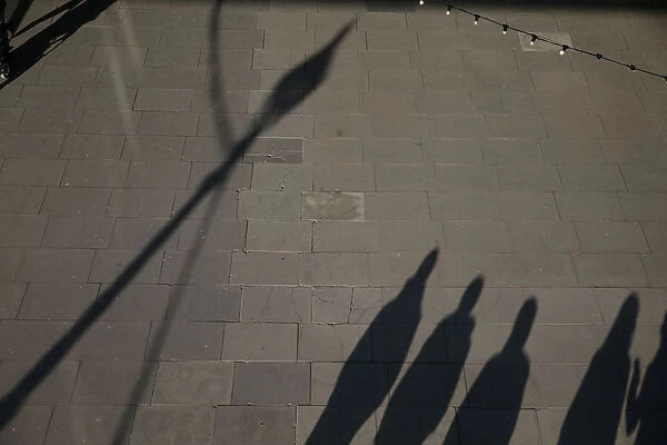 The shadows of pedestrians are cast on the pavement as they walk along the South Bank