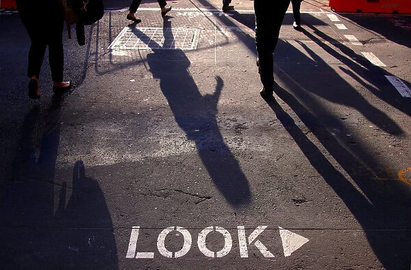Shoppers and workers cast shadows as they cross an intersection in the central business