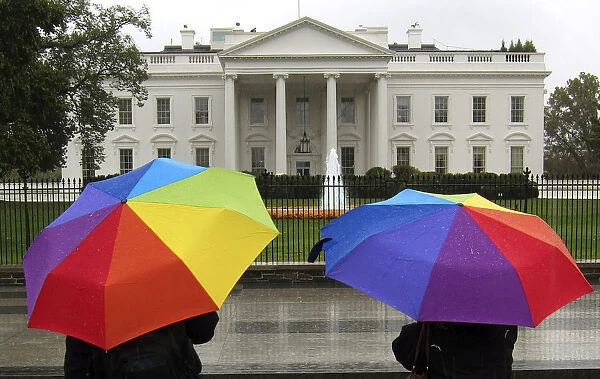 Sightseers holding umbrellas stop in front of the White House on a rainy day in