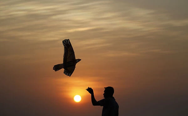 Silhouette of a vendor flying a kite is seen as he waits for customers during sunset