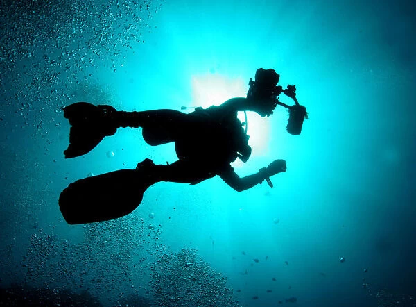 A silhouetted underwater photographer swims at a diving site near the island of Sipadan