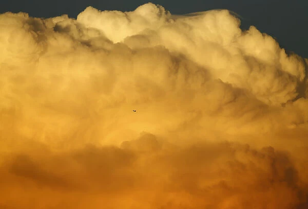 A small aircraft flies past a large emerging thunderstorm during sunset near Encinitas