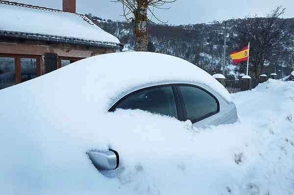 A snow covered car is parked next to a Spanish flag in Entrambasaguas
