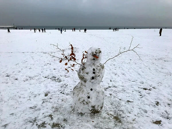 A snowman is seen as people stroll on a snow-covered beach in Gdynia