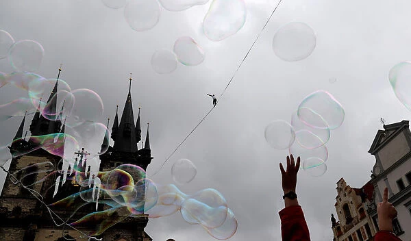 Soap bubbles float as a man balances on a line stretched over the Old Town Square in