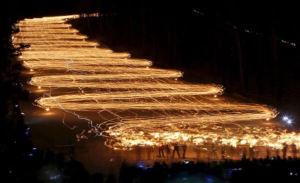 Spectators watch hundreds of skiers descend from a slope while holding lit torches in the