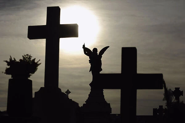 The sun is pictured behind a cross on a gravestone on the eve of All Saints Day