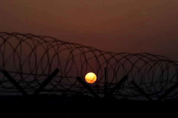 The sun rises over a barbed-wire fence at a checkpoint on the Grand Unification Bridge in