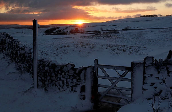 The sun rises over a snow covered footpath in Castleton