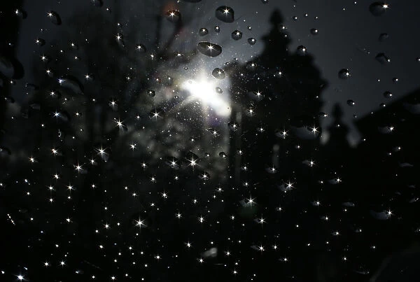 The sun is seen reflected in raindrops on a window after shower in London