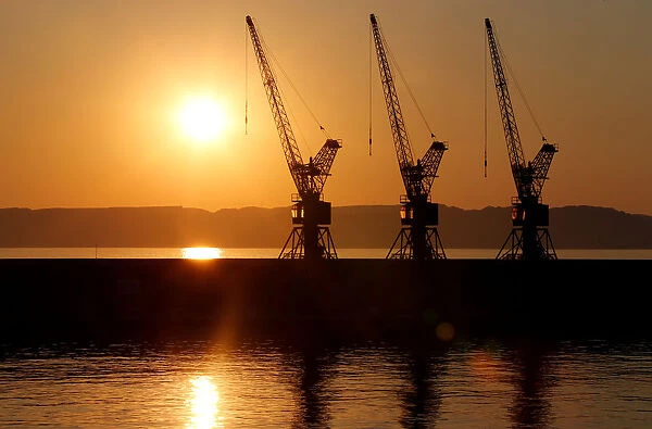 The sun sets behind loading cranes in the old harbour of Marseille