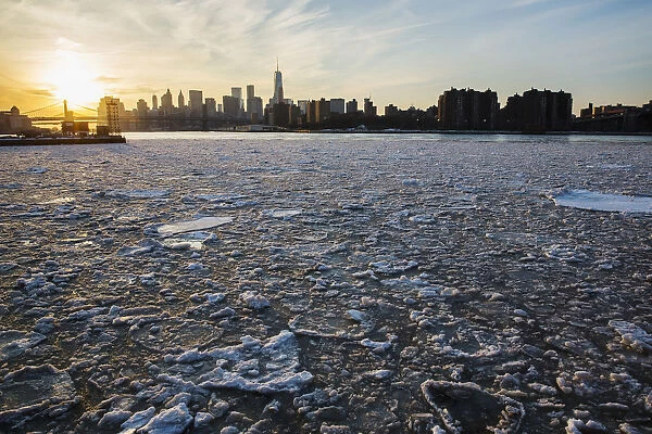 The sun sets behind the Manhattan skyline as ice floats down the East River in New York