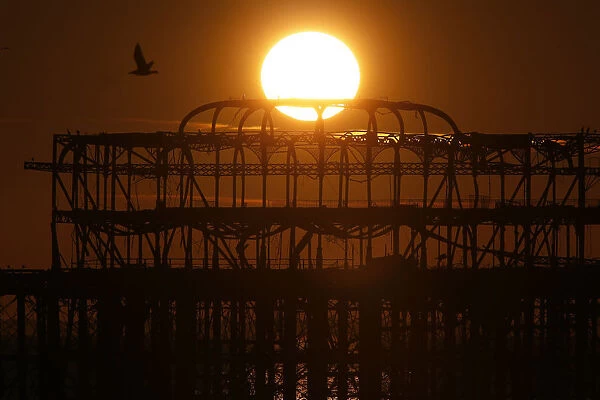 The sun sets behind the old West Pier in Brighton, southern England