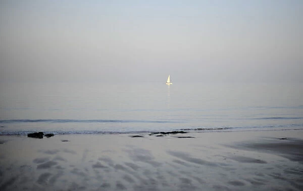 The sun sets on a small yacht in the north sea by a beach in Broadstairs in Kent