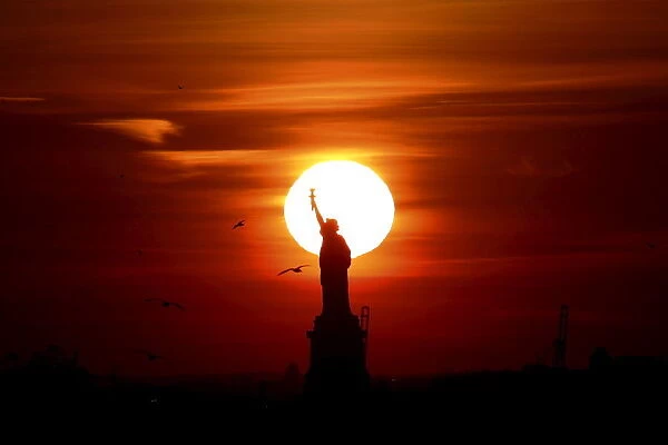 The sun sets behind the Statue of Liberty in New Yorks Harbor as seen from the Brooklyn