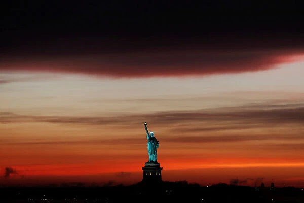 The sun sets behind the Statue of Liberty after a rain storm in New York