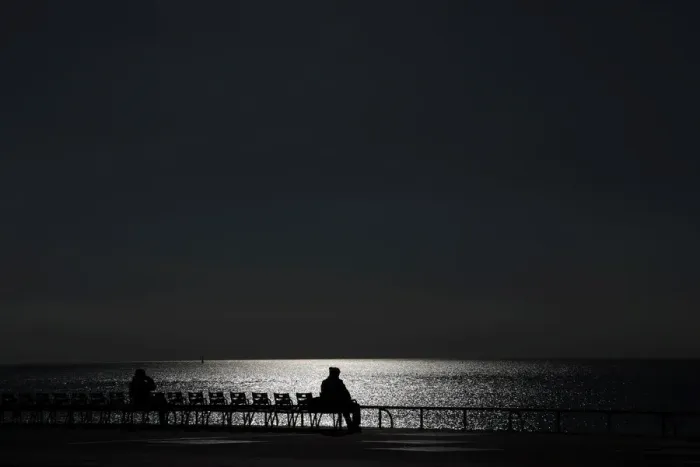 Framed Print : Sunlight reflects on the waters surface as people sit on chairs on a warm Framed Print : Sunlight reflects on the waters surface as people sit on chairs on a warm