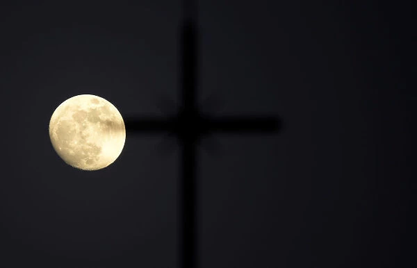 The super moon full moon is seen in front of the cross of a church in Siero