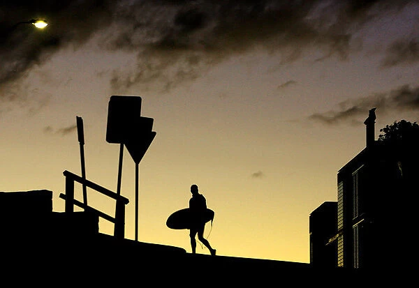 A surfer crosses the road with his board at sunset above Sydneys Bondi Beach