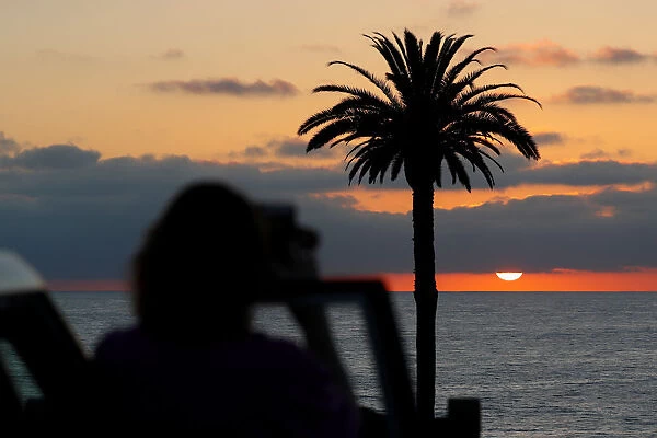 A tourist takes a picture of the setting sun at Moonlight Beach in Encinitas, California