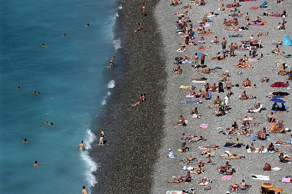 Tourists sunbathe and swim at the beach during a sunny summer day in Nice, southeastern