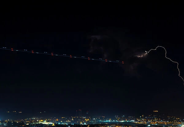 A trail left by a plane is seen near a lightning storm, seen from Mdina