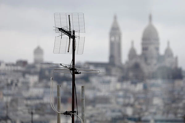 A tv antenna is seen on the rooftops of residential buildings in front of the Sacre Coeur