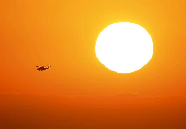 A U. S. military helicopter travels over the pacific ocean past a setting sun near Cardiff