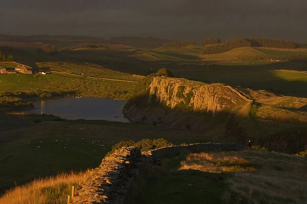 A walker looks north towards Scotland in late evening sun at Hadrians Wall near Crag