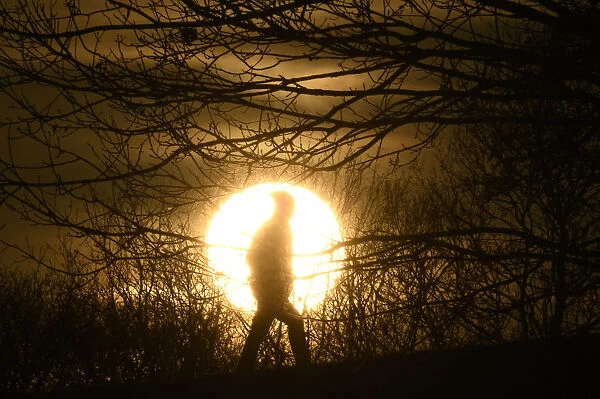 A walker is silhouetted in front of the setting sun on Primrose Hill in London